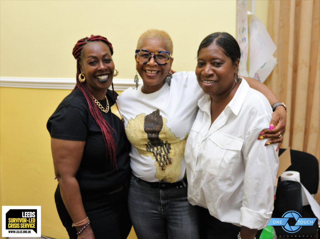 Three black women smiling at the camera and holding each other