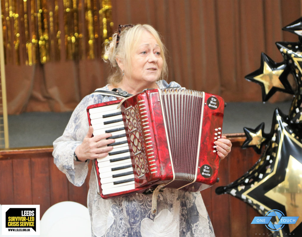 A white feminine person playing an accordion